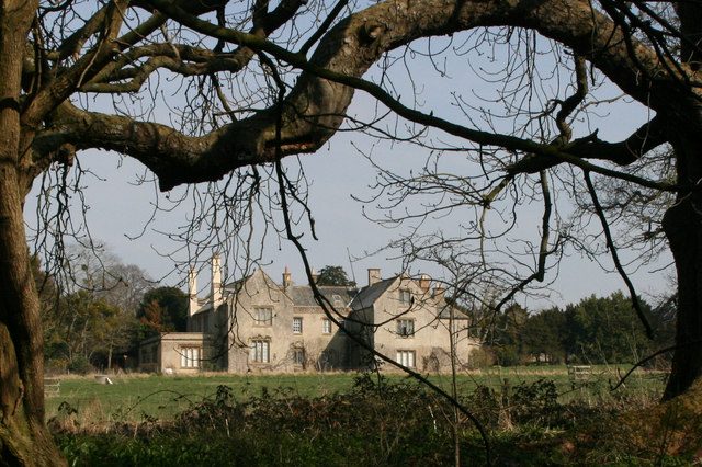 Poundisford Lodge, a gabled stone house seen across a stream and lawn